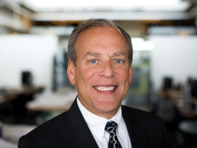 Lorne Eisen smiling while wearing a black blazer, white shirt and black and silver embossed tie