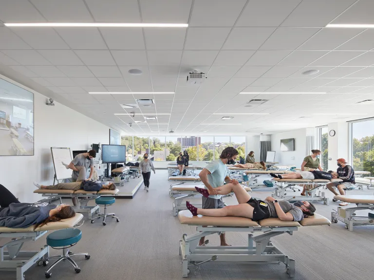 Students in a brightly lit medicine classroom practicing stretches with partners.