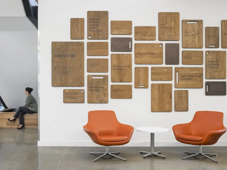 Interior of a nook with two women speaking, as well as a wall showcasing all of the donors to Mitchell Hall on cutting boards engraved on a wall