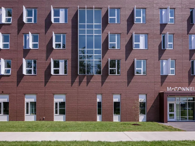 Exterior of McConnell Hall, framed to showcase every window's shade open with the front entrance on the bottom right corner