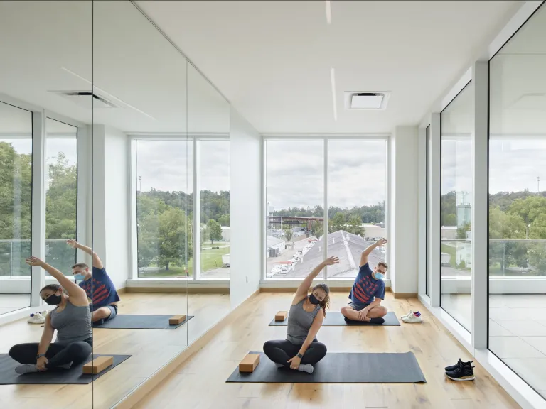 Interior of an upper floor yoga space with a mirrored wall and two people in a seated yoga stretch