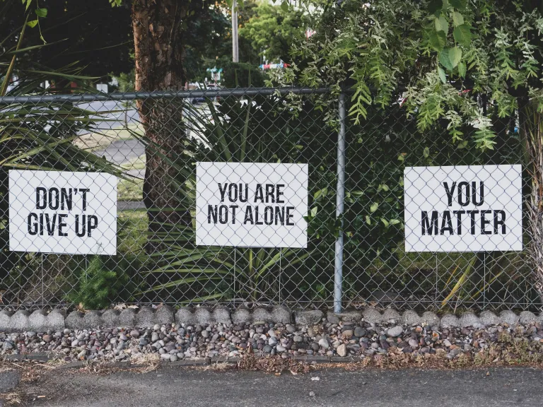 Three signs behind a fence that read "Don't Give Up," "You Are Not Alone," and "You Matter."