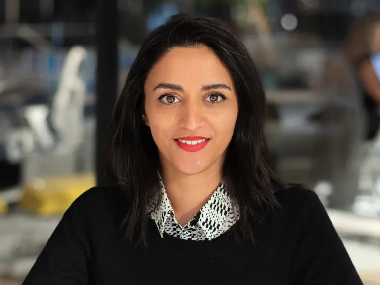 Parva Markiw smiling, wearing a black sweater with grey button down underneath