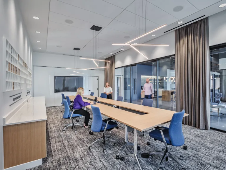 Modern conference room with very long maple table, glass walls, and varied bar hanging lights