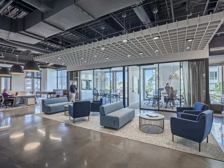 Interior of a modern workplace with all glass conference rooms, couches and chairs that are gray and blue.