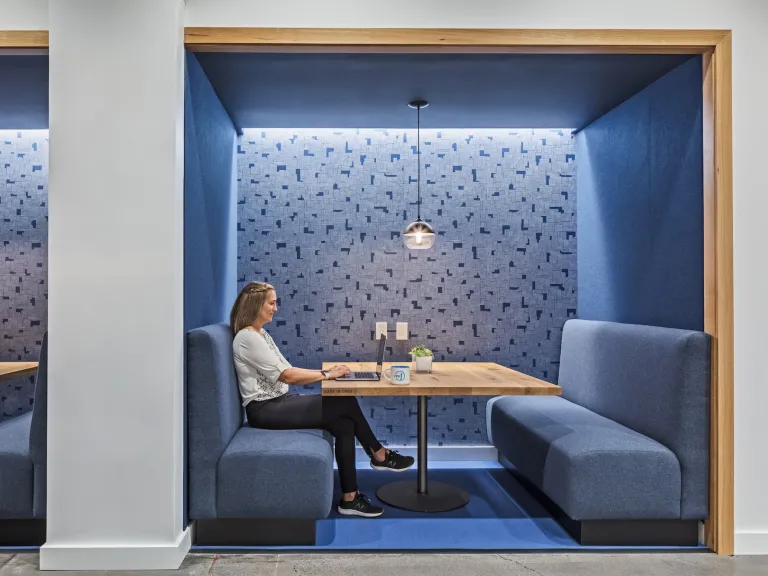 Woman sitting in an inset booth style workspace with blue walls and cushions