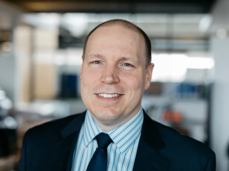 Rick Rodman smiling, wearing a navy blazer and blue striped shirt with navy tie