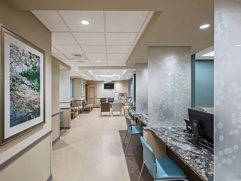 Interior hallway with check in desks to the right and waiting room further down to the left, featuring beige and light blue accents