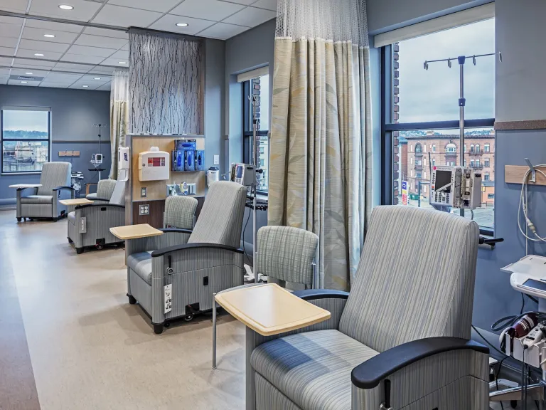 Interior of a patient space with multiple cushioned chairs with arm tables and curtain dividers