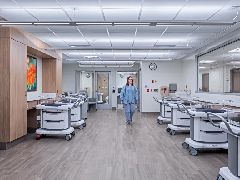 Nursery space in Care Center with multiple crib carts and nurse walking down the middle