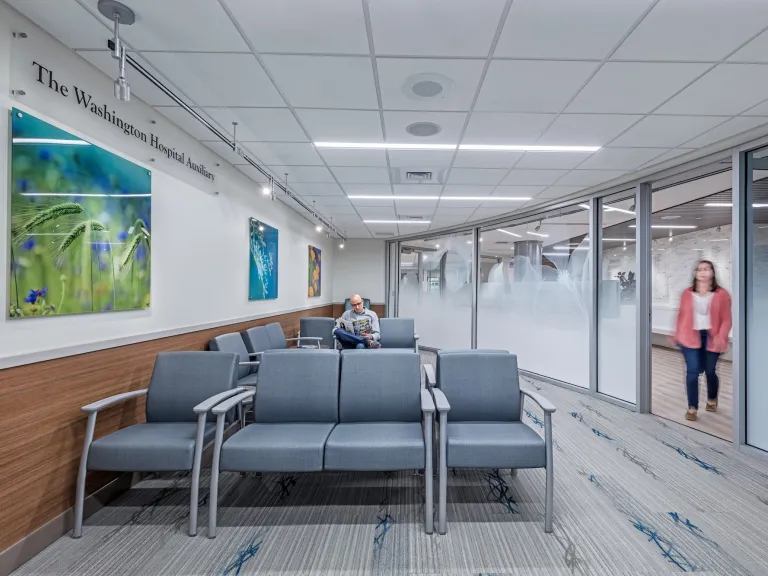 Waiting room space in Care Center, featuring padded chairs, glass entrance wall and blue and green wall art
