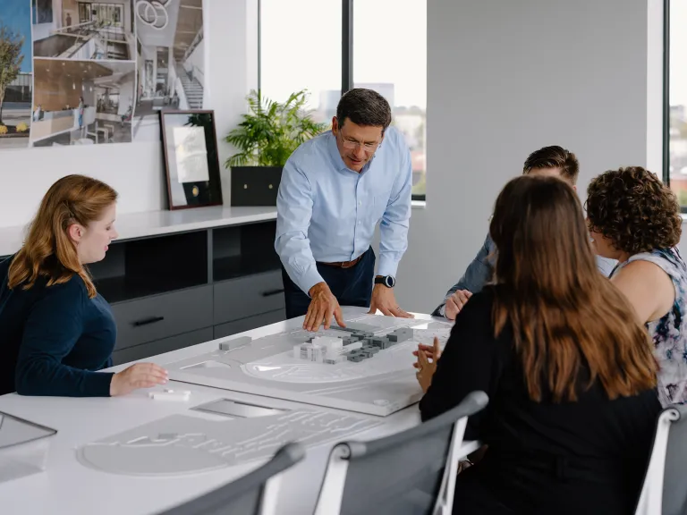 Group of people around a table working on and discussing architectural plans and a model.