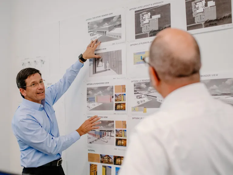 Two people discussing renderings pinned up on a board.