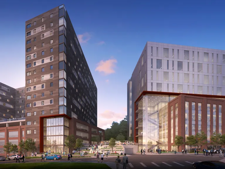 Exterior view of two tall mixed used buildings in the evening with many people walking around them.