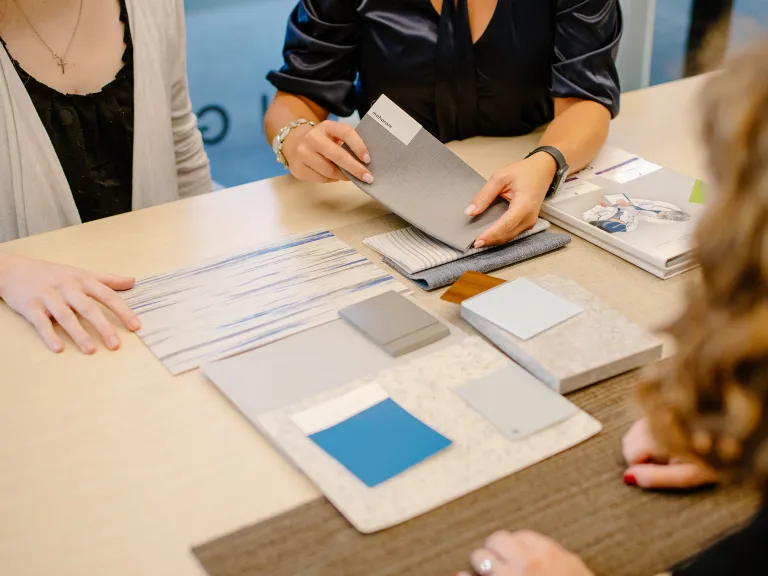 Group of people sitting at a table with fabric and paint swatches.
