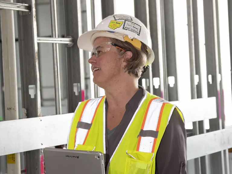 Person in a hardhat and construction garments holding a clipboard.