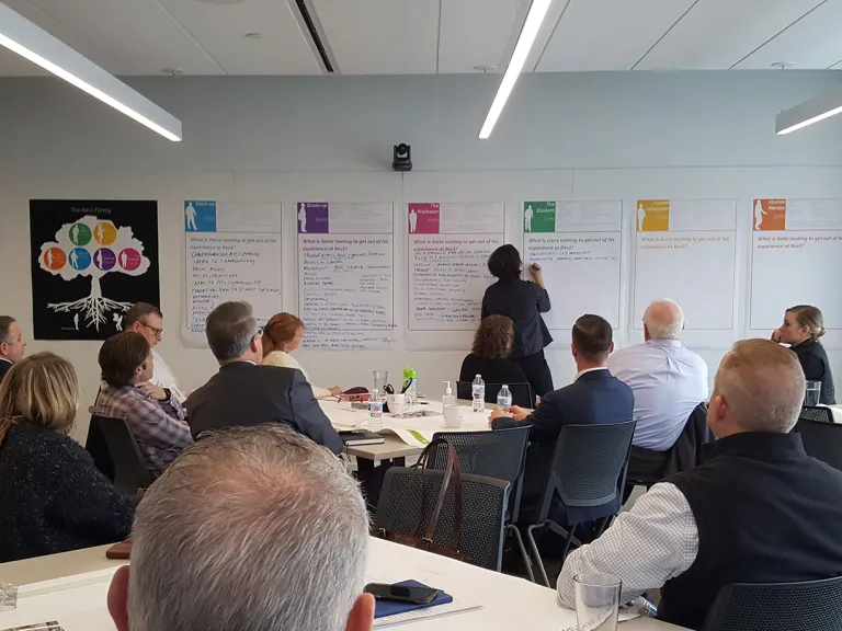 Group of people at tables participating in a visioning workshop and writing on user persona worksheets.