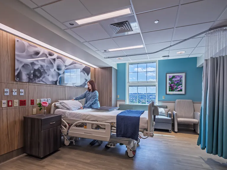 nurse fluffs pillow in hospital patient room