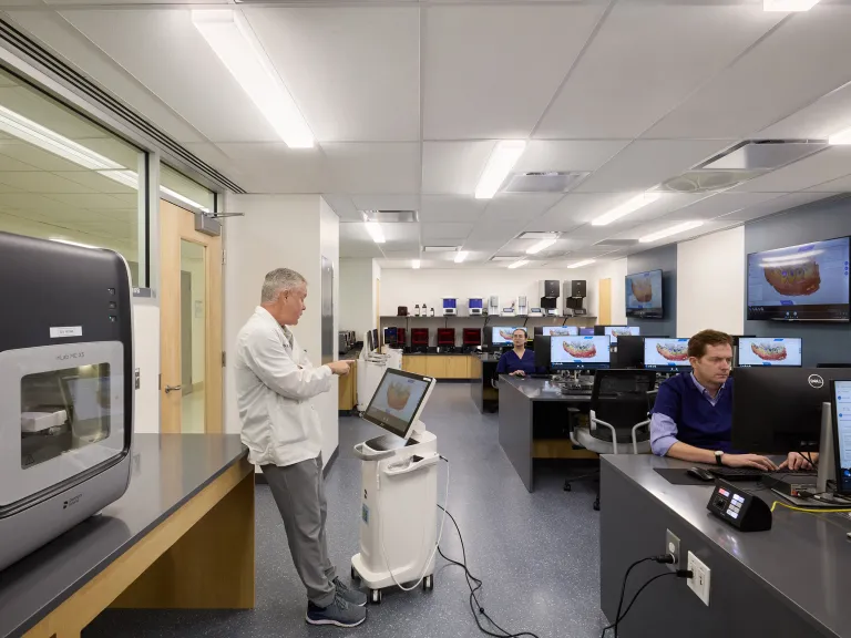 professor wearing lab coat in classroom with computers and dental equipment