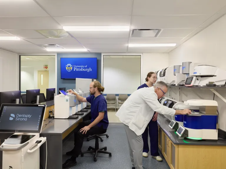 professor wearing lab coat and students wearing scrubs in classroom with dental equipment
